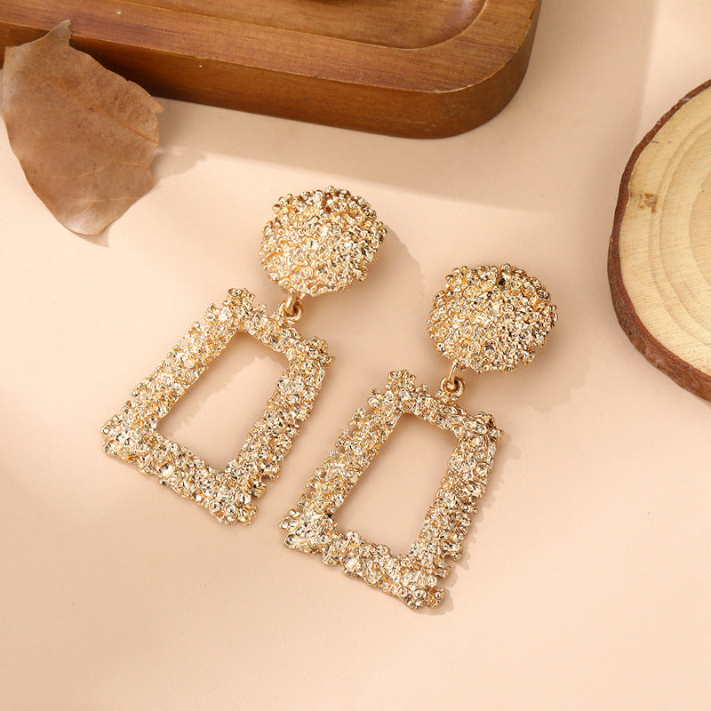 Gold earrings with geometric designs on a beige surface