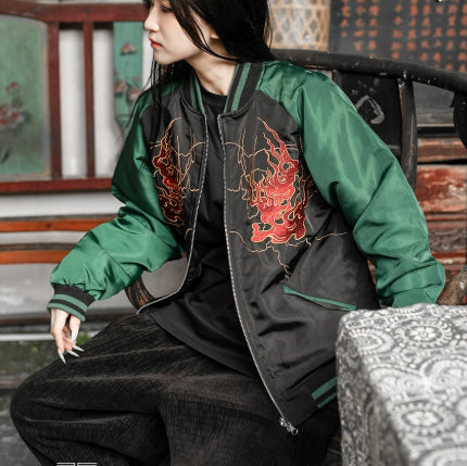 Person wearing a green and black jacket with embroidered designs, sitting outdoors.