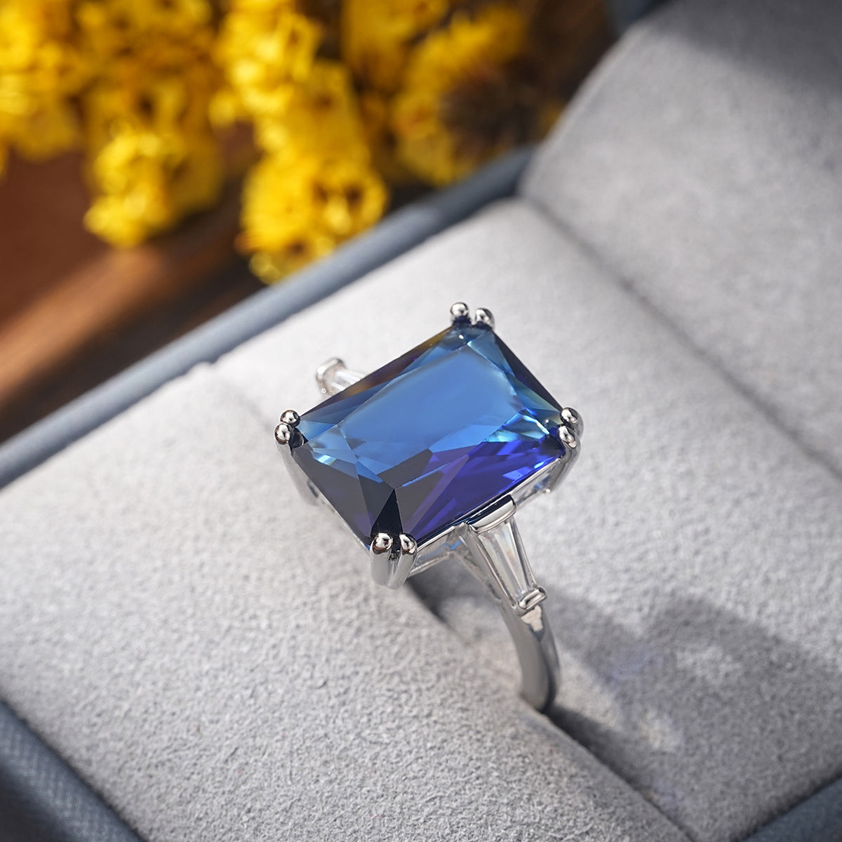 Blue gemstone ring on a soft surface with yellow flowers in the background, mordenstore. 