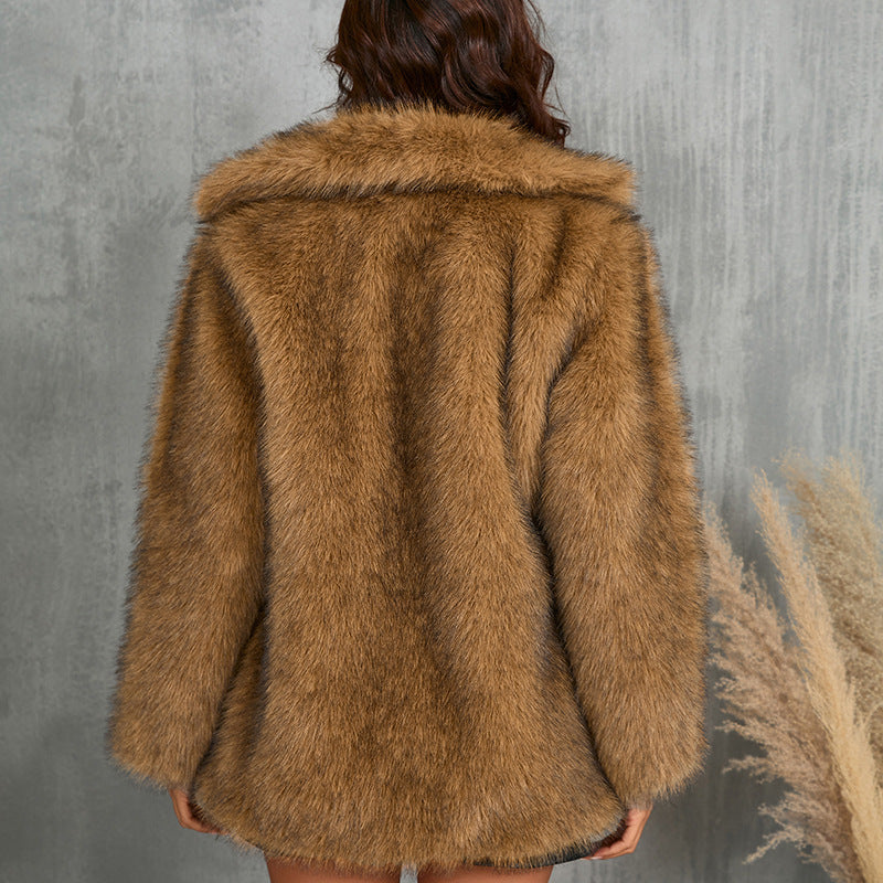 Brown faux fur coat worn by a person against a gray concrete wall.