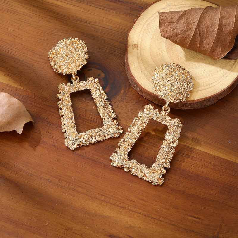 Gold earrings on a wooden surface with leaves