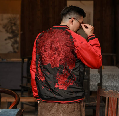 Person wearing a red and black jacket with intricate designs, standing in a room with wooden furniture and a painting.