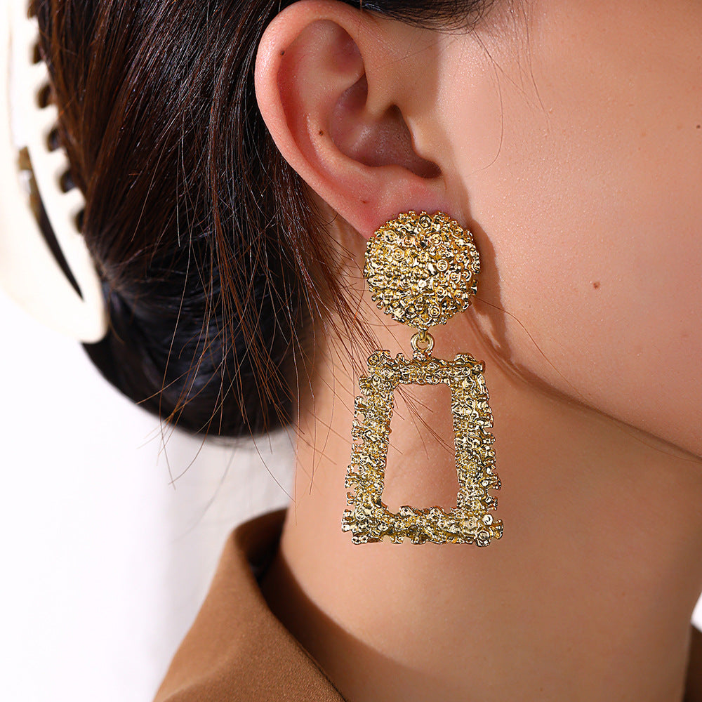 Gold earrings worn by a person with a neutral background